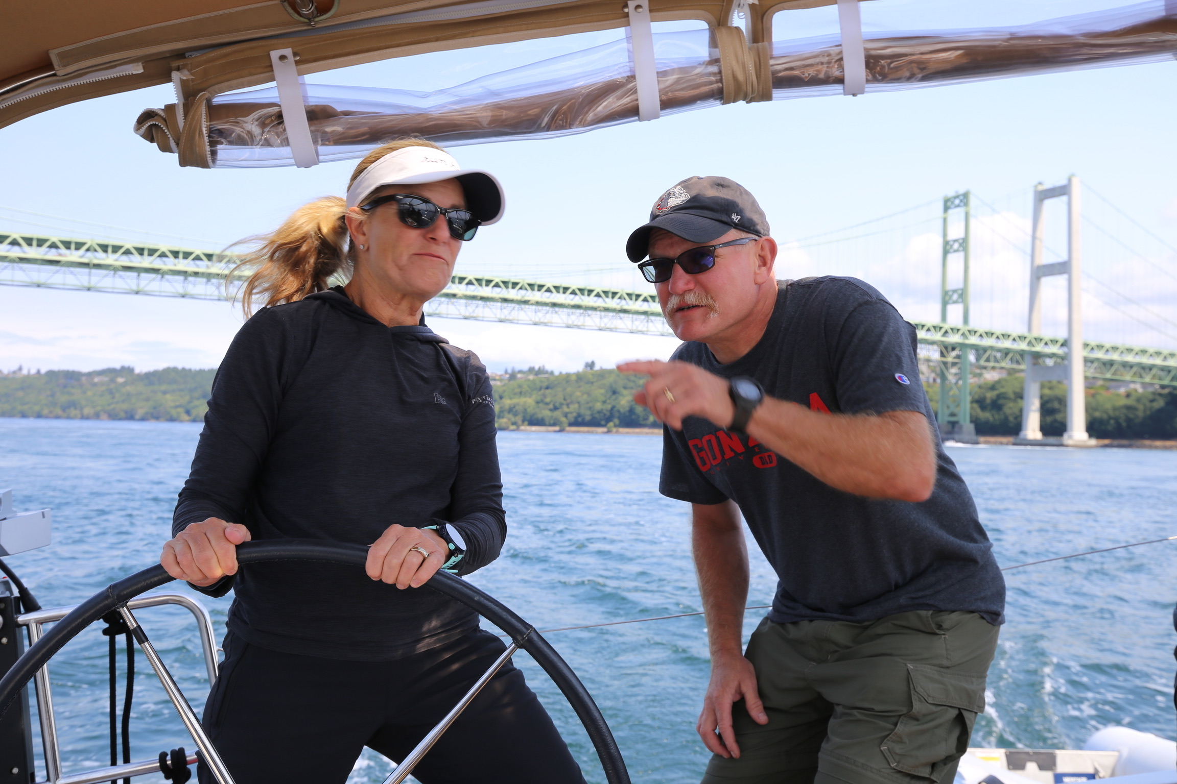 Two sailors talking at the helm near a bridge.